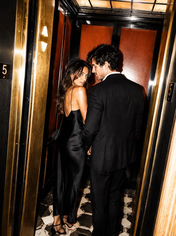 A couple dressed up, glancing back at each other stepping into an elevator