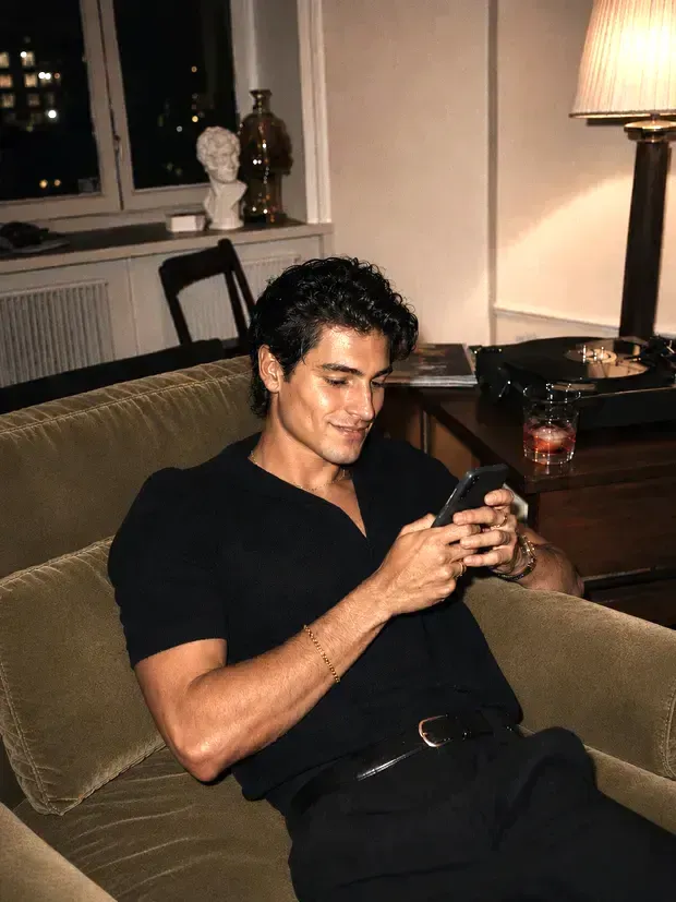 Man smirking at his phone while texting on a sofa at night