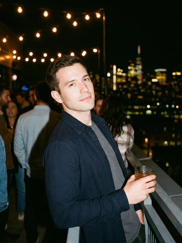 AI-generated photo of the same man from the selfies, at a rooftop bar at night